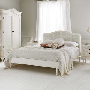 May include: White wooden bed frame with a woven headboard and a white bedspread. The bed is in a bedroom with white walls and white curtains.