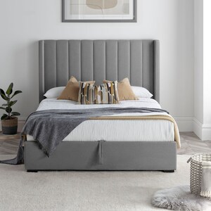 May include: A grey upholstered bed frame with a tufted headboard and a storage compartment. The bed is made up with a white duvet, a grey throw blanket, and decorative cushions.