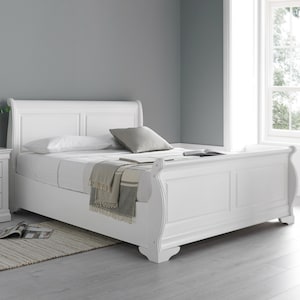 May include: A white wooden sleigh bed with a headboard and footboard. The bed has a mattress, pillows, and a blanket. The bed frame has a curved design. The room also features a rug and a nightstand. The bed is approximately 200 cm long.
