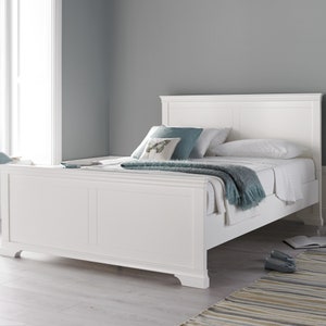 May include: White wooden bed frame with a headboard and footboard. The bed is made with white bedding and a blue throw blanket.