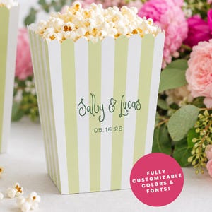 May include: Two popcorn boxes filled with popcorn, featuring green and white stripes. The boxes are personalised with the names "Sally & Lucas" and the date "05.16.26". A bouquet of pink flowers is in the background.