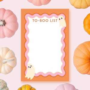 Puede incluir: Una lista de tareas con temática de Halloween con el texto "TO-BOO LIST" en naranja y rosa. La lista está rodeada por un borde ondulado y presenta dos fantasmas de dibujos animados. El fondo es rosa claro con varias calabazas.