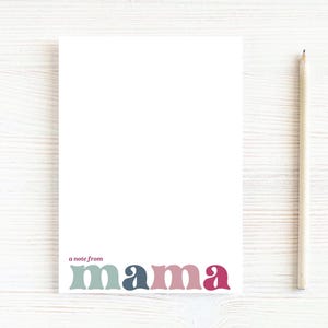 May include: A white notepad with the text "a note from mama" in a retro font. The word "mama" is in shades of teal, navy, pink, and magenta. A wooden pencil rests on the right side of the notepad.