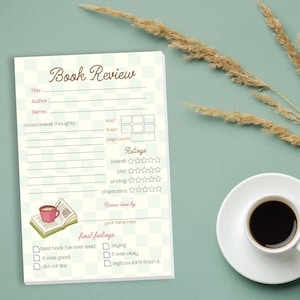 May include: A notepad with a "Book Review" title, featuring sections for title, author, genre, and notes. Includes a rating section with stars and a space for final feelings. A cup of coffee sits on a white saucer.