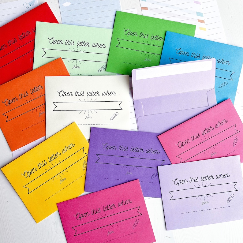 May include: A set of ten colorful envelopes with the text "Open this letter when." printed on each one. The envelopes are arranged in a random pattern on a white surface.