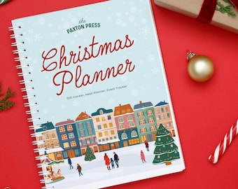 Puede incluir: Un planificador navideño con encuadernación en espiral y cubierta azul claro. La portada muestra el texto "Christmas Planner" en escritura roja, una ilustración de ciudad, copos de nieve y el texto "Gift tracker, Meal Planner, Event Tracker."