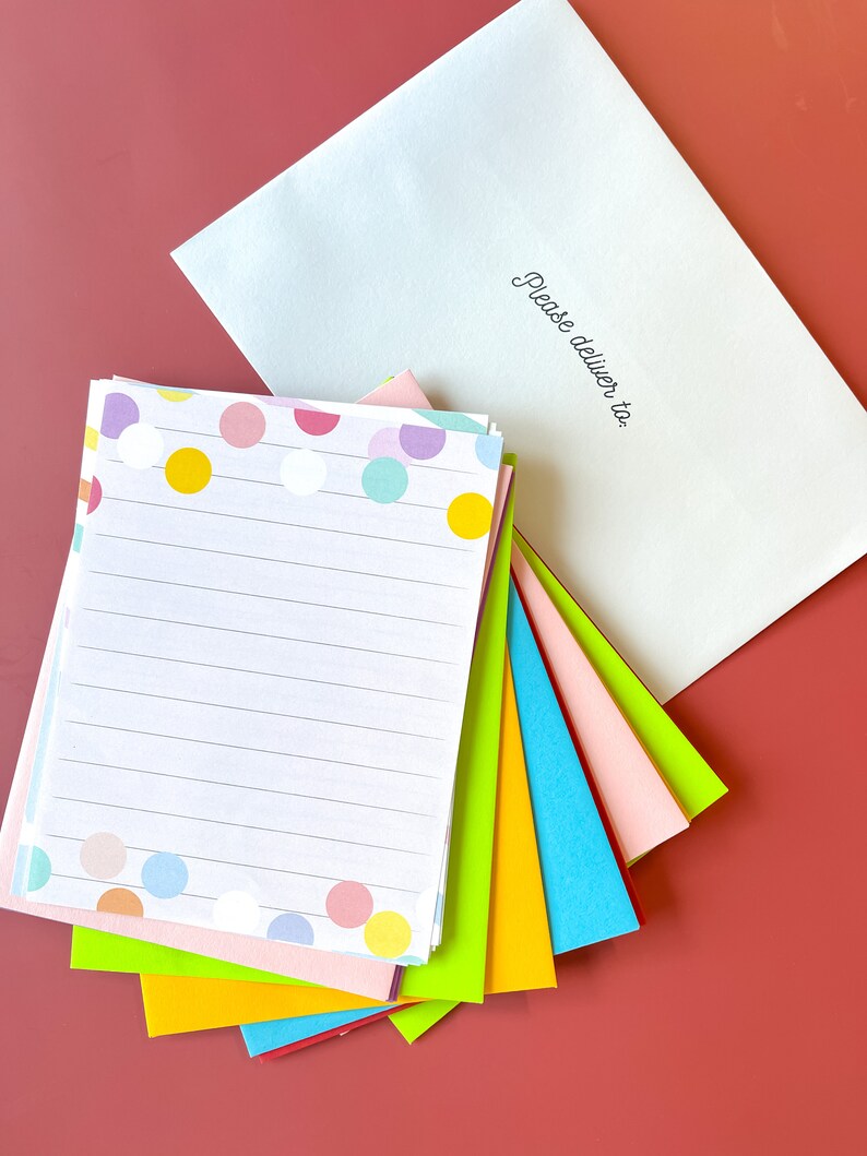 May include: A stack of colorful stationery paper with a polka dot pattern and lined writing paper. The top sheet has a white background with colorful polka dots. The paper is folded in half and has a white envelope with the text "Please deliver to:" on the front.
