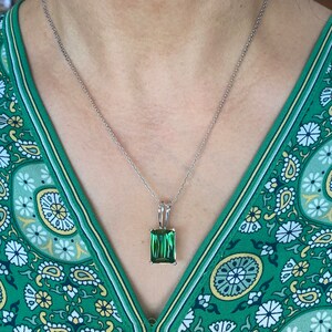 May include: A silver necklace with a rectangular, emerald-green gemstone pendant. The pendant is set in a silver frame and hangs from a delicate silver chain. The necklace is displayed against a green patterned background.