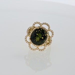 May include: A gold ring with a large oval green gemstone surrounded by a halo of smaller diamonds. The ring has a delicate floral design.
