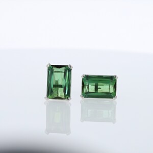 May include: A pair of emerald green gemstone earrings with a rectangular cut. The earrings are set in silver.