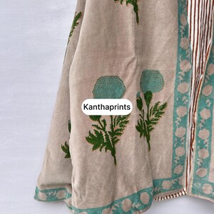 May include: Beige fabric with green floral and leaf patterns. The fabric has a teal border with white floral designs. The text "Kanthaprints" is visible on the fabric. The right side of the fabric has vertical stripes in brown and white.