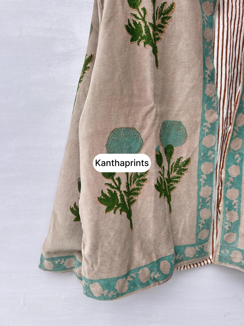 May include: Beige fabric with green floral and leaf patterns. The fabric has a teal border with white floral designs. The text "Kanthaprints" is visible on the fabric. The right side of the fabric has vertical stripes in brown and white.