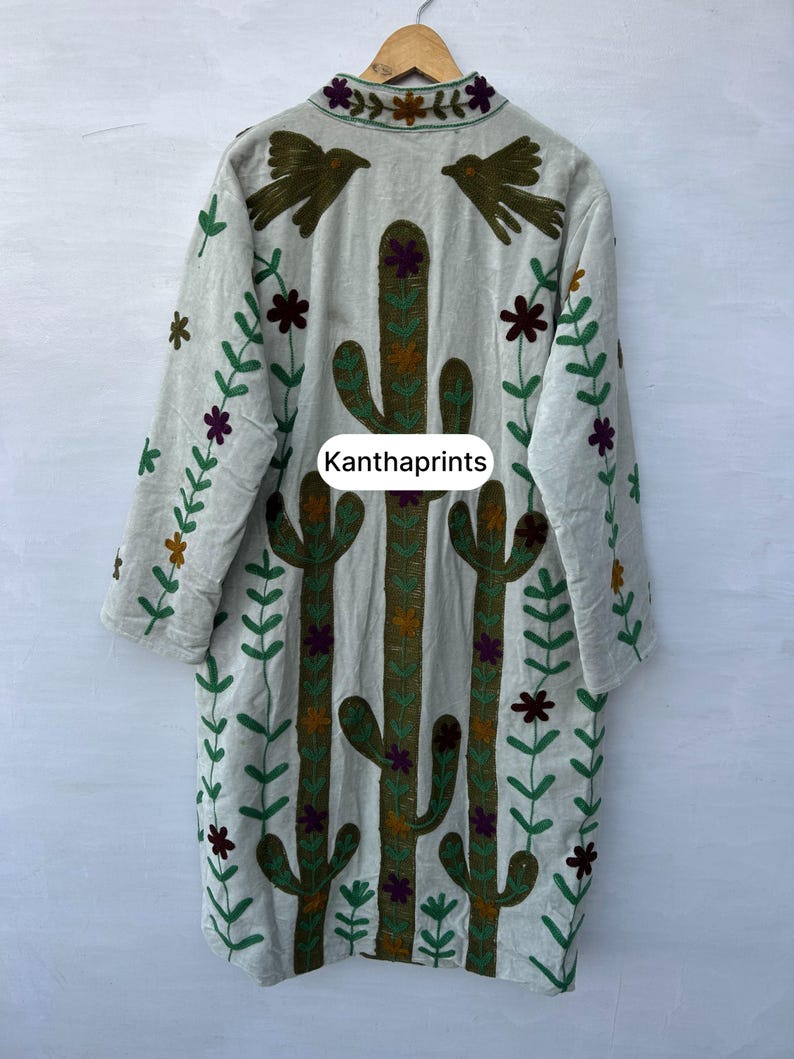 May include: A light gray embroidered coat with a cactus and floral design. The coat features long sleeves and a collar with bird and flower embroidery. The text "Kanthaprints" is visible on the front.