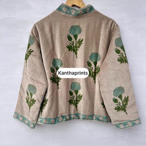 May include: Beige jacket with a high collar and long sleeves, adorned with teal floral patterns and green leaves. The jacket features teal trim along the collar and hem. The text "Kanthaprints" is visible on the front.