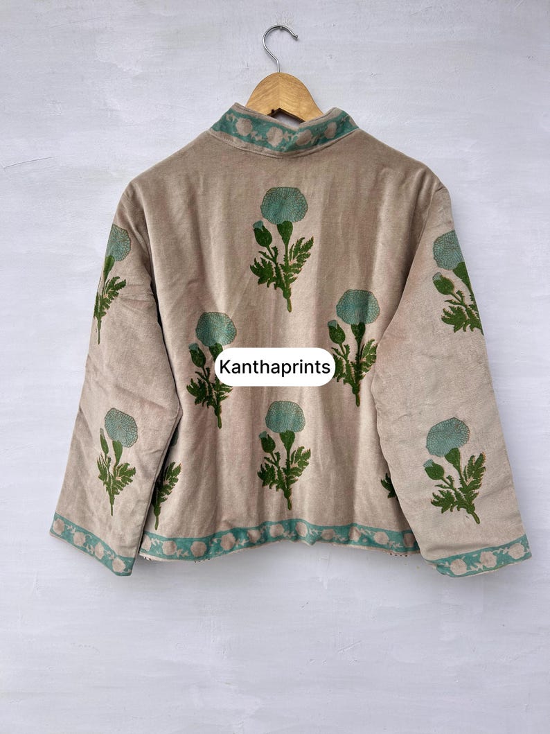 May include: Beige jacket with a high collar and long sleeves, adorned with teal floral patterns and green leaves. The jacket features teal trim along the collar and hem. The text "Kanthaprints" is visible on the front.