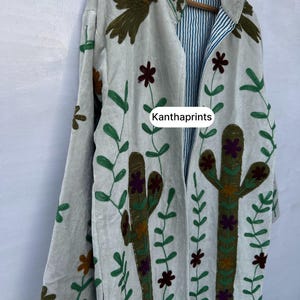 May include: A light gray embroidered jacket with a botanical design. The jacket features a cactus, flowers, and bird embroidery in green, brown, and purple. The inside lining has blue and white stripes. The text "Kanthaprints" is visible.