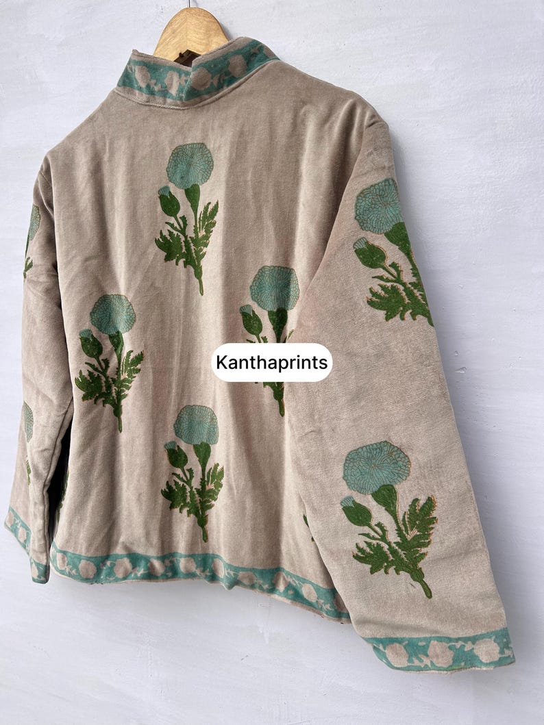 May include: Beige jacket with a high collar and long sleeves, adorned with a repeating pattern of teal floral designs and green leaves. The trim and collar feature a teal and white pattern. The text "Kanthaprints" is visible on the jacket.