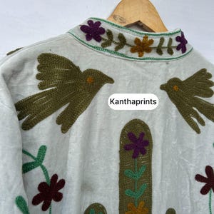 May include: Off-white jacket with embroidered details. Features a cactus and bird design in shades of green, brown, purple, and orange. The collar is decorated with floral embroidery. The text "Kanthaprints" is visible.