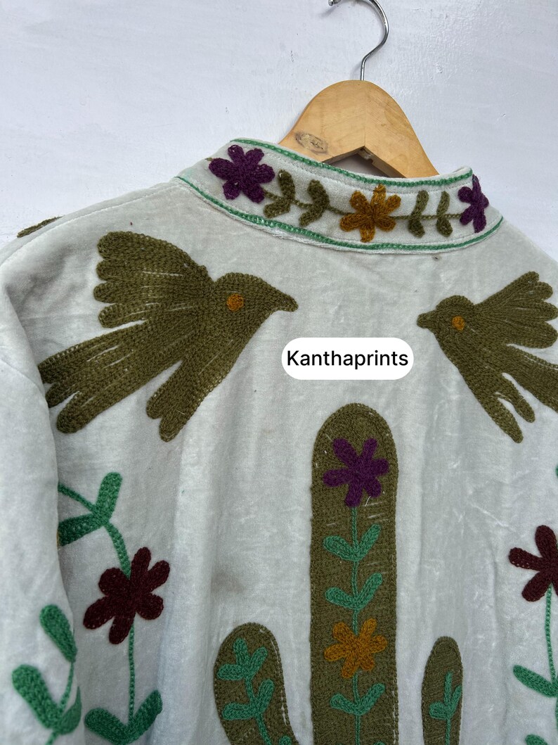 May include: Off-white jacket with embroidered details. Features a cactus and bird design in shades of green, brown, purple, and orange. The collar is decorated with floral embroidery. The text "Kanthaprints" is visible.