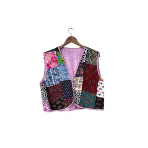 May include: A patchwork vest with a variety of fabric patterns and colors, including floral, paisley, and geometric designs. The vest has a pink striped lining and is hanging on a wooden hanger.