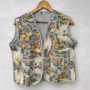 May include: A sleeveless vest with a floral and bird pattern, hanging on a wooden hanger. The vest features a gray background with a repeating design of yellow fruit, pink flowers, and white birds. The interior lining is striped.