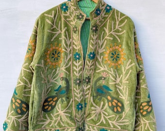 May include: A green velvet jacket with intricate embroidery featuring peacock and floral designs. The jacket has a mandarin collar and a striped green lining. The embroidery includes shades of yellow, blue, and beige, creating a detailed and artistic look.