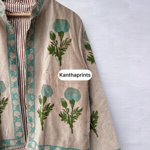 May include: Beige jacket with a floral print in teal and green. The jacket has a teal border and a striped brown and white lining. The text "Kanthaprints" is visible on the jacket.