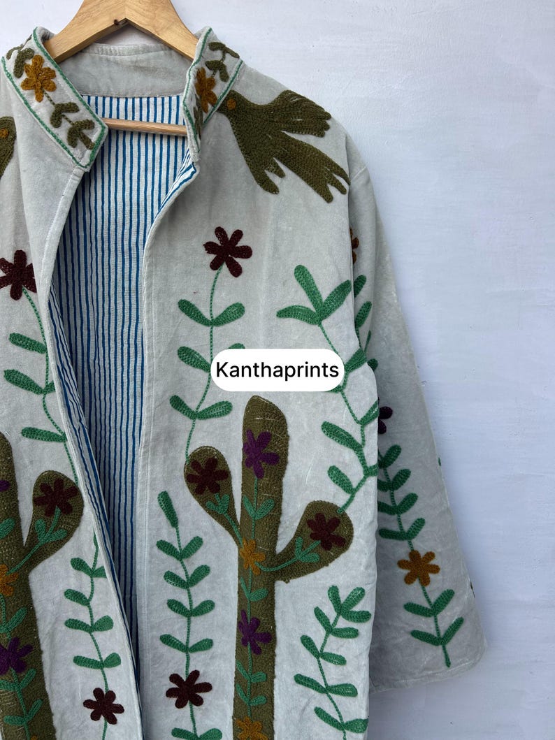 May include: Off-white jacket with embroidered floral and cactus designs in green, brown, and purple. The jacket has a striped blue and white lining and the text "Kanthaprints".