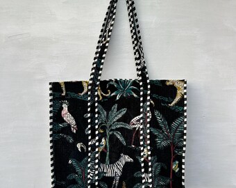 May include: Black tote bag with a jungle-themed pattern featuring zebras, parrots, and palm trees. The bag has a checkered pattern on the straps and edges. The bag is designed with a rectangular shape and two handles.