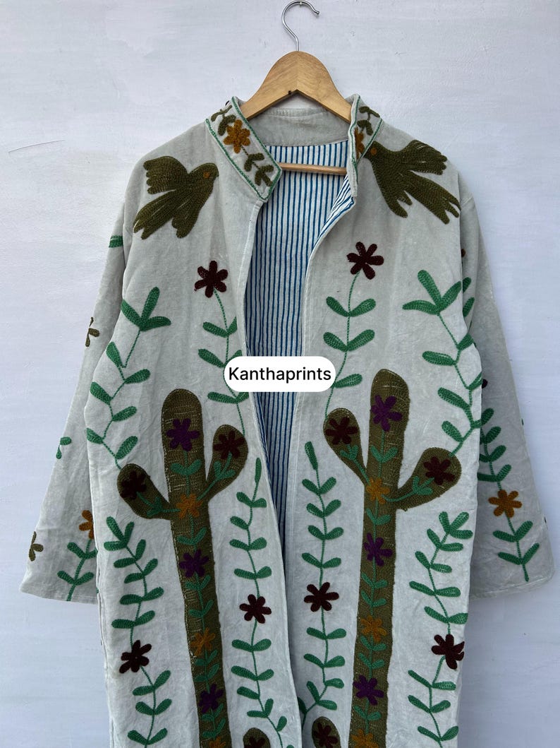 May include: A light-colored, long-sleeved jacket with embroidered cactus and floral designs. The jacket features a striped interior and is adorned with green and brown bird and flower motifs. The text "Kanthaprints" is visible on the jacket.
