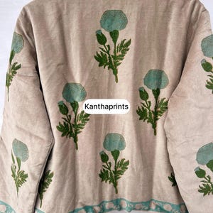 May include: Beige jacket with a floral pattern in teal and green. The jacket has a high collar and teal trim. The text "Kanthaprints" is printed on the jacket.