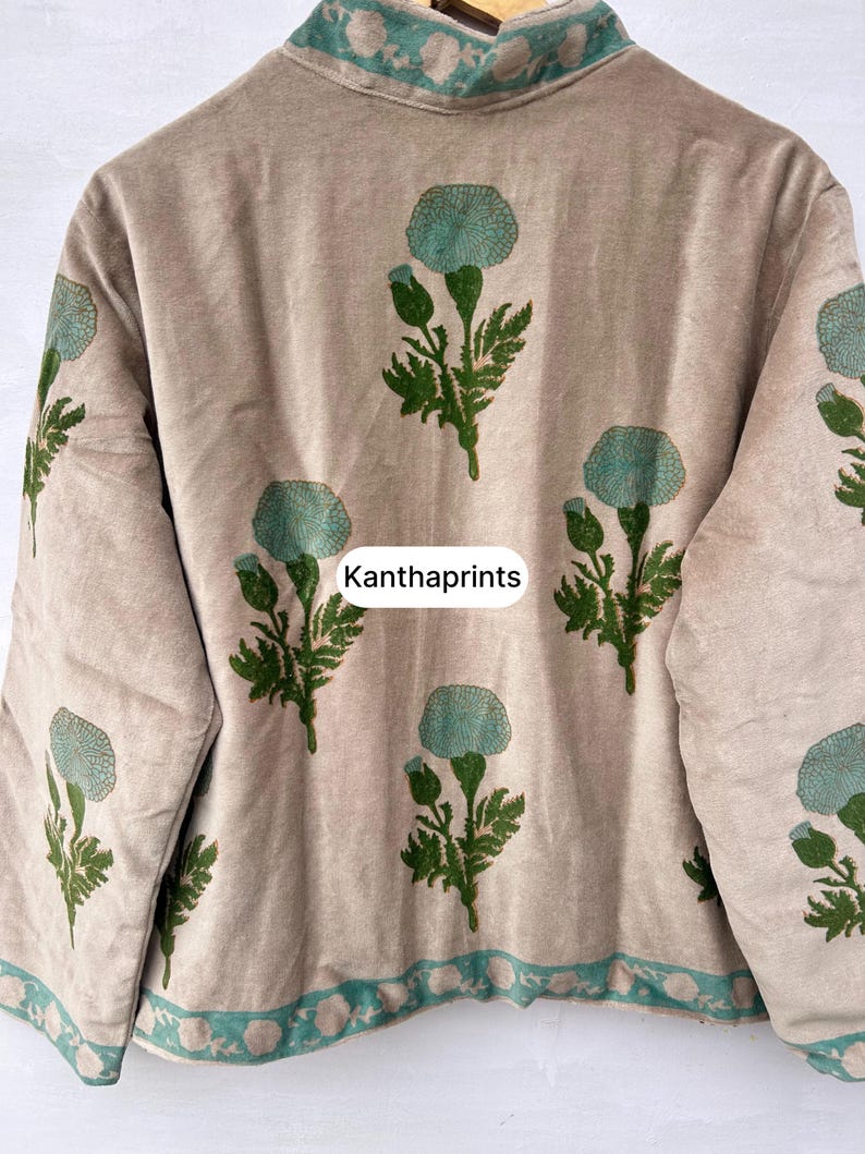 May include: Beige jacket with a floral pattern in teal and green. The jacket has a high collar and teal trim. The text "Kanthaprints" is printed on the jacket.