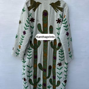 May include: A light gray embroidered coat with a cactus and floral design. The coat features long sleeves and a collar with bird and flower embroidery. The text "Kanthaprints" is visible on the front.