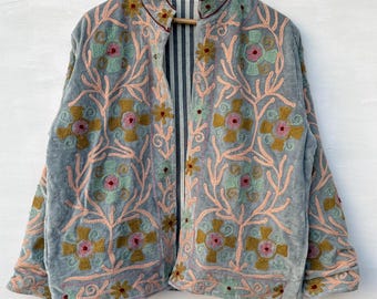May include: A light blue embroidered jacket with a floral design. The jacket features pink, green, and gold floral embroidery on the front and sleeves. The jacket is hanging on a wooden hanger against a white background.