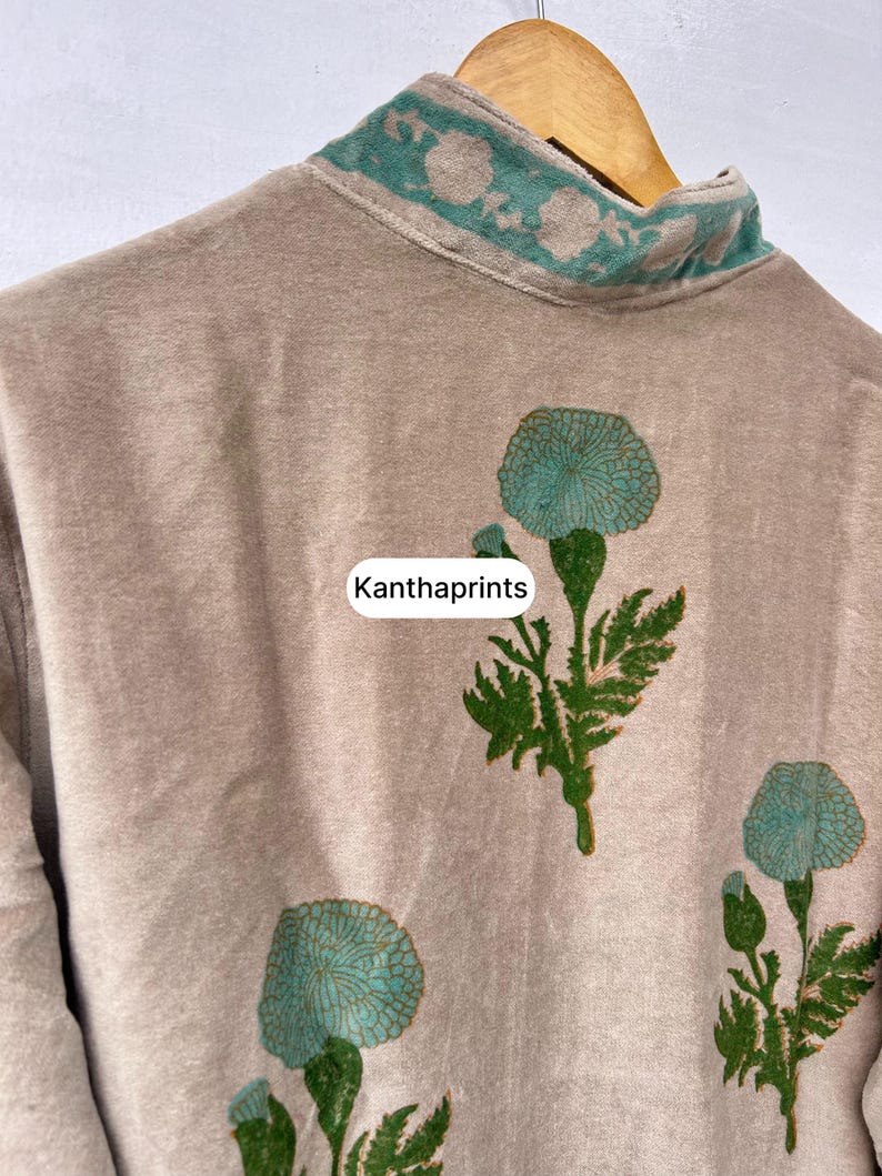 May include: A beige garment with a high collar and floral embroidery in teal. The garment features teal floral designs on the front. The text "Kanthaprints" is visible on the garment.
