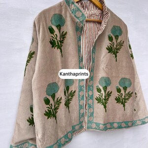 May include: Beige jacket with a floral design in teal and green. The jacket has a teal border and a striped interior. The text "Kanthaprints" is visible on the front of the jacket.