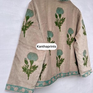 May include: Beige jacket with a floral pattern in green and teal. The jacket has a high collar and is decorated with a repeating floral design. The text "Kanthaprints" is visible on the front of the jacket.