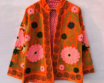 May include: An orange embroidered jacket with pink and green floral designs. The jacket features a red and white striped lining and is displayed on a wooden hanger. The floral embroidery includes large pink flowers and smaller green and black accents.