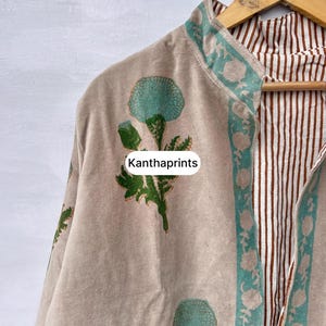 May include: Beige jacket with a floral print in teal and green. The jacket has a teal border with a floral design and a brown and white striped interior. The text "Kanthaprints" is visible on the jacket.