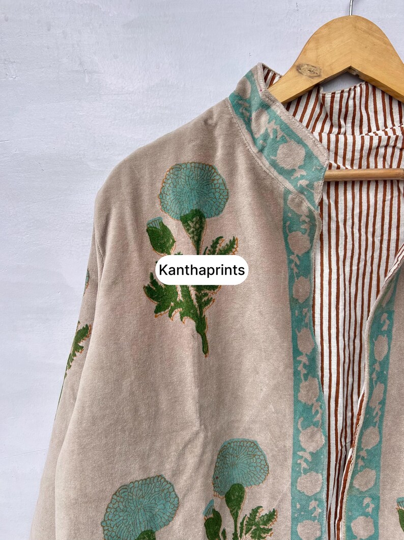 May include: Beige jacket with a floral print in teal and green. The jacket has a teal border with a floral design and a brown and white striped interior. The text "Kanthaprints" is visible on the jacket.
