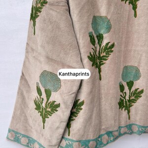 May include: Beige fabric with a floral pattern in teal and green. The design features stylized flowers and leaves, with a teal border along the edge. The text "Kanthaprints" is visible on the fabric.