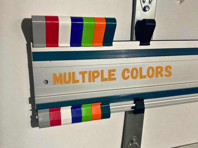 Pu&ograve; includere: Un righello in metallo argentato e verde acqua con un gancio nero a ciascuna estremit&agrave;. Il righello ha un'etichetta che dice "MULTIPLE COLORS" in lettere arancioni. Il righello ha una fila di punte in plastica colorate in alto e in basso, tra cui grigio, rosso, bianco, blu, verde, arancione e nero.