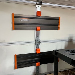 Pu&ograve; includere: Due scaffali di stoccaggio per garage Ridgid neri e arancioni montati su una porta da garage bianca. Gli scaffali sono in metallo e hanno una superficie testurizzata. Gli scaffali sono progettati per contenere strumenti e altri oggetti.