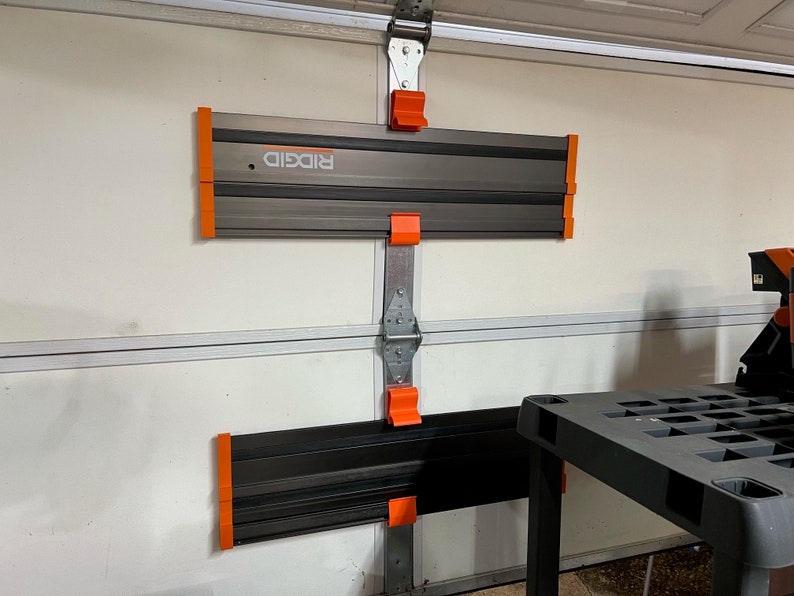 Pu&ograve; includere: Due scaffali di stoccaggio per garage Ridgid neri e arancioni montati su una porta da garage bianca. Gli scaffali sono in metallo e hanno una superficie testurizzata. Gli scaffali sono progettati per contenere strumenti e altri oggetti.