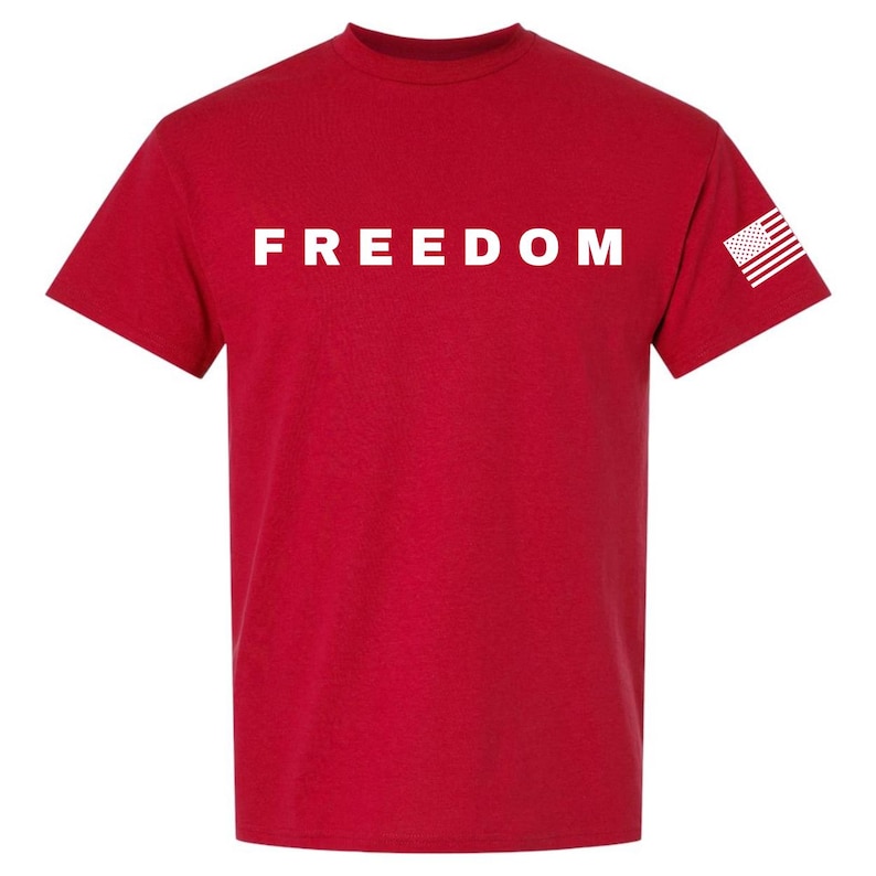 May include: A red t-shirt with the word "FREEDOM" printed in white across the chest. The American flag is printed on the right sleeve. This tee is a patriotic statement.