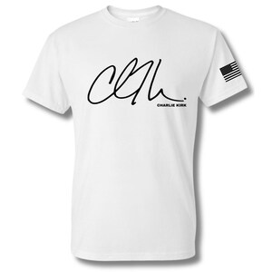 May include: White t-shirt featuring a black signature and the text "CHARLIE KIRK". An American flag is printed on the right sleeve. The shirt is made of a soft, comfortable material.