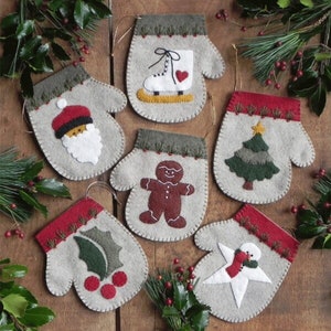 Può includere: Sei addobbi natalizi in feltro a forma di guanti, ognuno con un diverso design festivo: un omino di pan di zenzero, un albero di Natale, un pupazzo di neve, una foglia di agrifoglio, Babbo Natale e un pattino da ghiaccio. I guanti sono tutti grigi con accenti rossi e verdi.