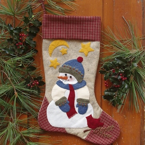 May include: A beige Christmas stocking with a snowman applique. The snowman is wearing a blue hat, a red scarf, and blue mittens. The stocking has a red and white plaid cuff and a red cardinal applique.