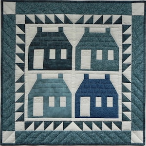 May include: A quilt with a blue and white colour scheme featuring four houses with white windows and doors. The quilt is framed with a white and blue border with a scalloped edge.