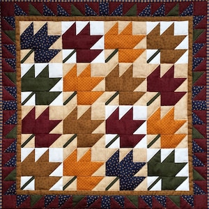 May include: A quilt featuring a pattern of autumn leaves in shades of brown, orange, red, green, and blue. The leaves are arranged in a repeating pattern, creating a visually appealing design.
